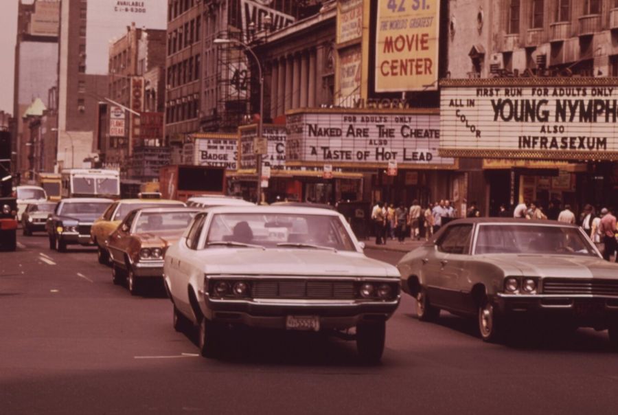 Cars on 42nd Street in Manhattan passing a row of cinemas whose marquees advertise first-run films for adults only