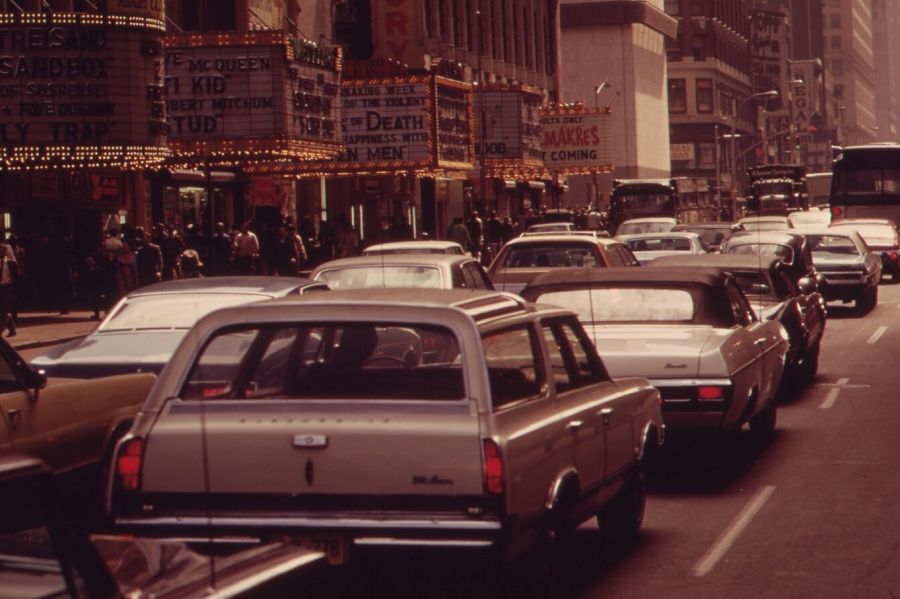 Traffic on 42nd Street in Manhattan, with crowds on the pavement under a row of illuminated cinema marquees advertising adult and action films