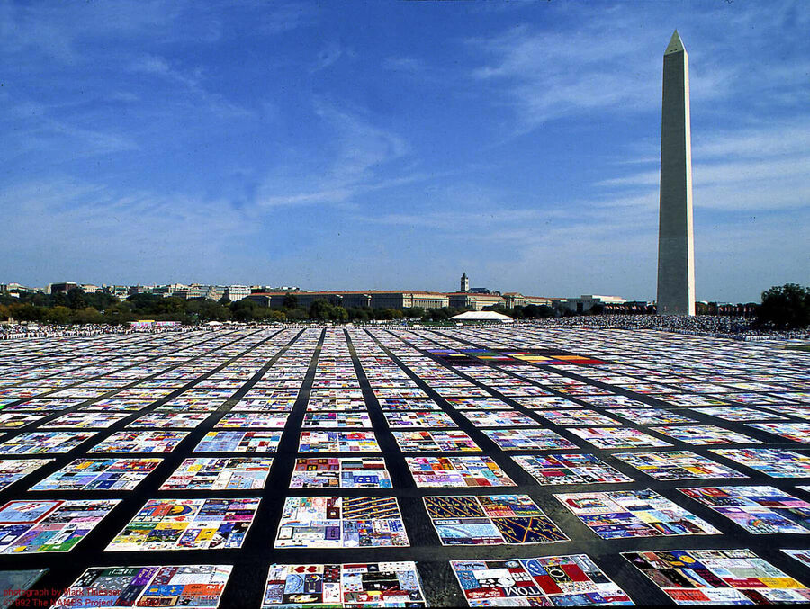 Thousands of colourful quilt panels laid out in rows on the grass of the National Mall, with the Washington Monument rising on the right