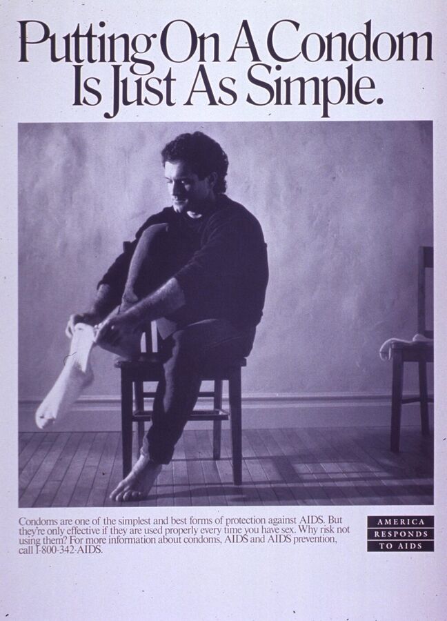 Black and white poster with the headline Putting On A Condom Is Just As Simple above a photograph of a man sitting on a chair pulling on a sock