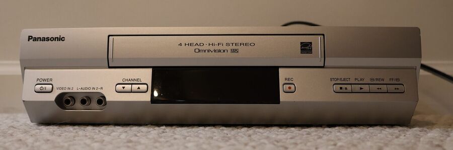 Front of a silver Panasonic VHS video recorder with a cassette slot, a small display and a row of buttons