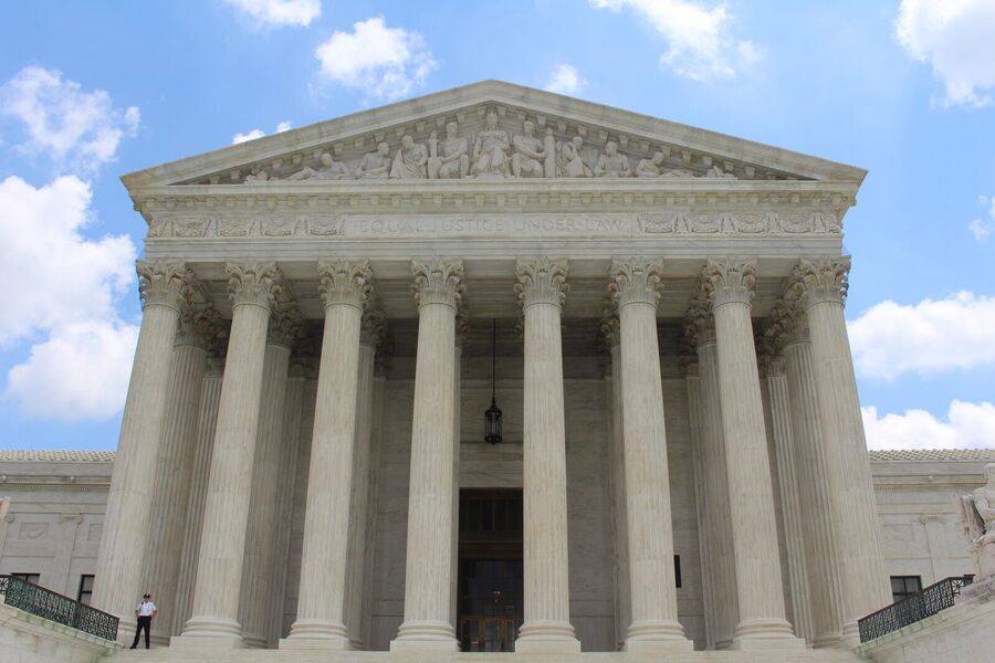 The white marble columns and carved pediment of the United States Supreme Court building under a blue sky with clouds