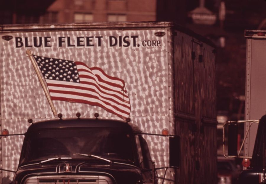 The front of a delivery truck with a large painted American flag on its box, parked on a city street