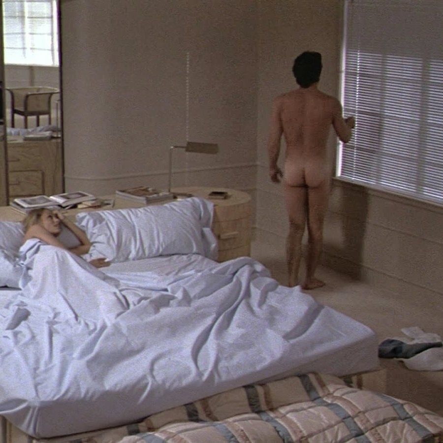 Film still of Richard Gere naked, seen from behind, looking out of a window with venetian blinds while a woman lies in the bed