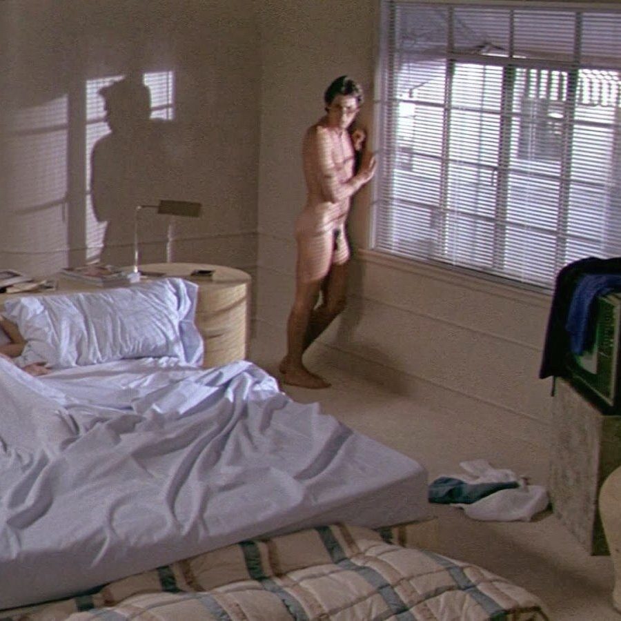 Film still of Richard Gere standing naked by a window with venetian blinds in a sunlit bedroom, an unmade bed in the foreground