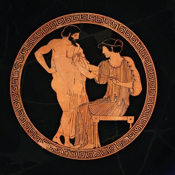 Round red-figure vase picture of a bearded man in a cloak standing before a seated woman who touches his chest