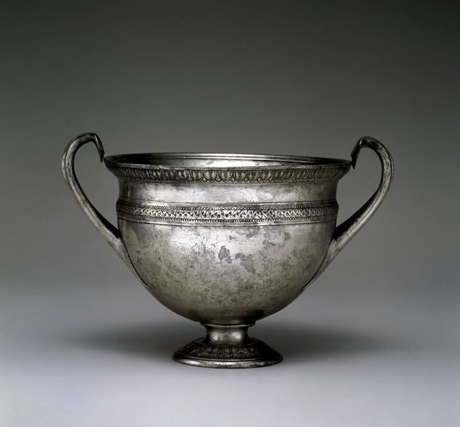 Plain Roman silver drinking cup with two curved handles and a narrow foot, decorated with bands of ornament around the rim
