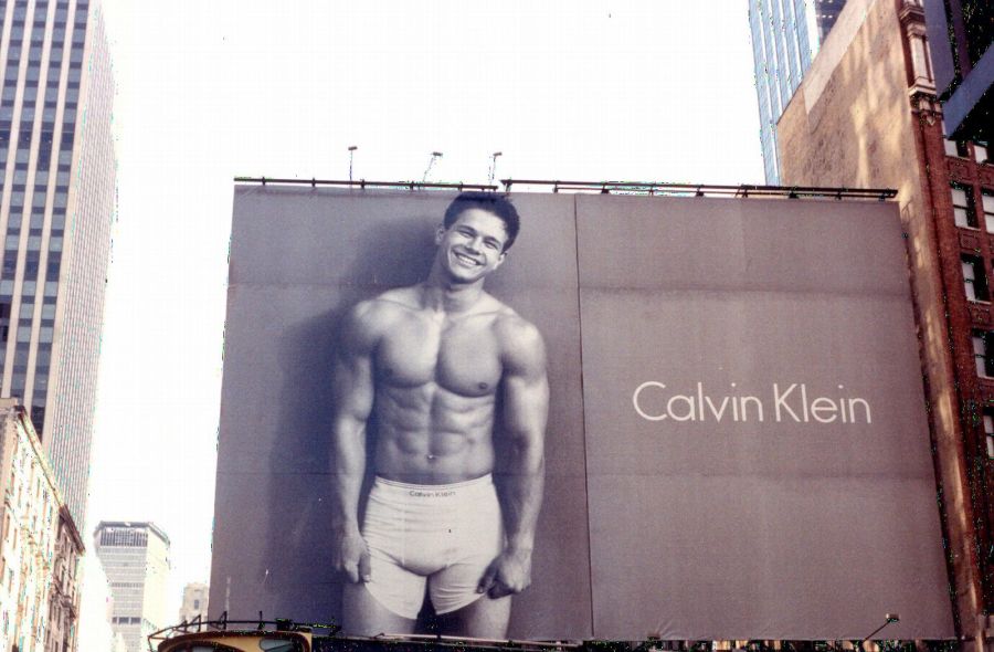 A huge Calvin Klein billboard between Manhattan towers, showing a smiling, muscular young man bare-chested in white boxer briefs