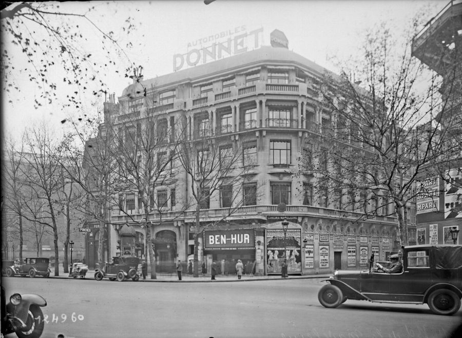 Black and white photograph of a large Paris corner building with a cinema on the ground floor advertising Ben-Hur, a 1920s car parked in front and bare trees