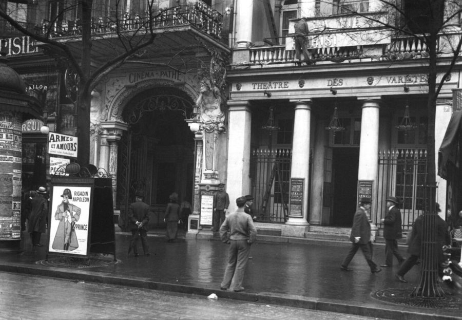 Black and white street photograph of an ornate cinema entrance marked Cinéma Pathé next to a theatre with columns, with passers-by on the pavement