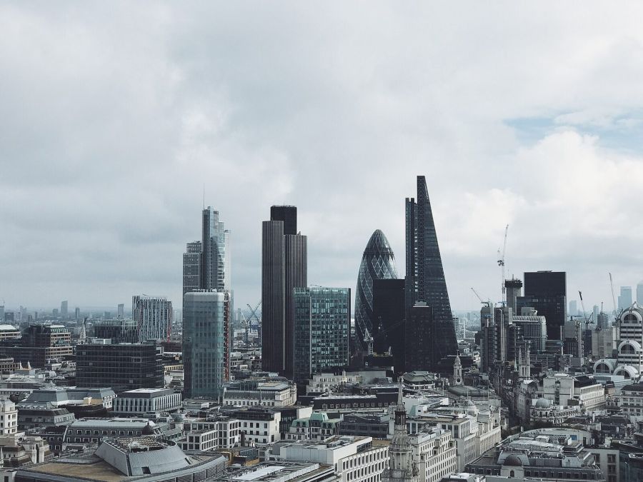 The towers of the City of London, including the rounded Gherkin and the angular Cheesegrater, rising above older stone buildings under a cloudy sky