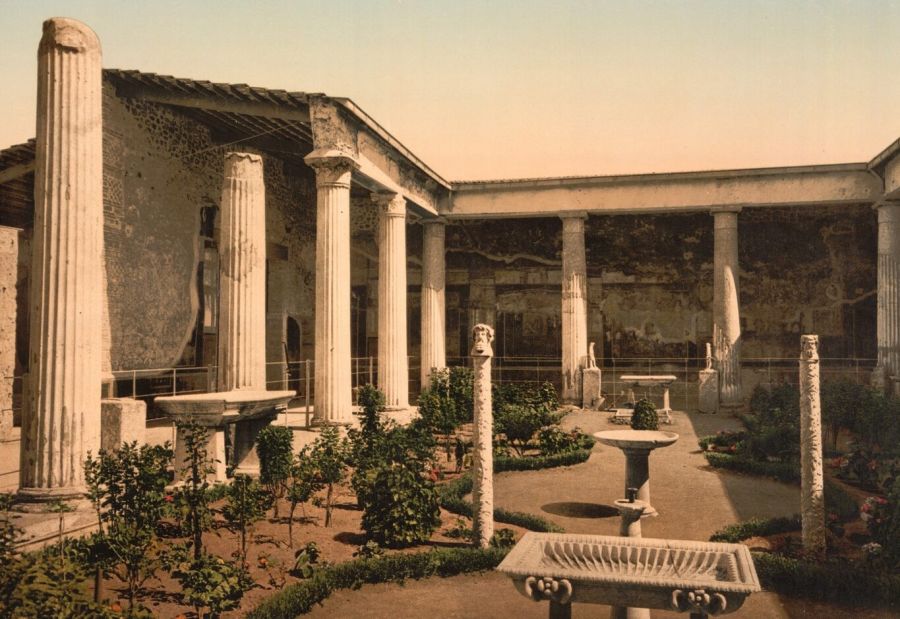 Colour print of a Pompeian courtyard with white columns, marble basins and a replanted garden, the walls painted red and black