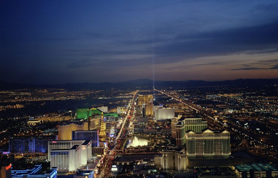Aerial view at dusk of a long avenue of brightly lit hotels and casinos stretching towards the horizon under a dark blue sky