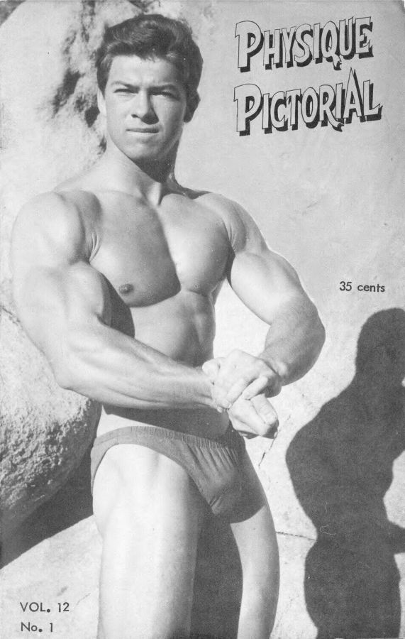 Magazine cover with the title Physique Pictorial showing a muscular young man in brief trunks with his arms crossed in front of him, standing against a rock