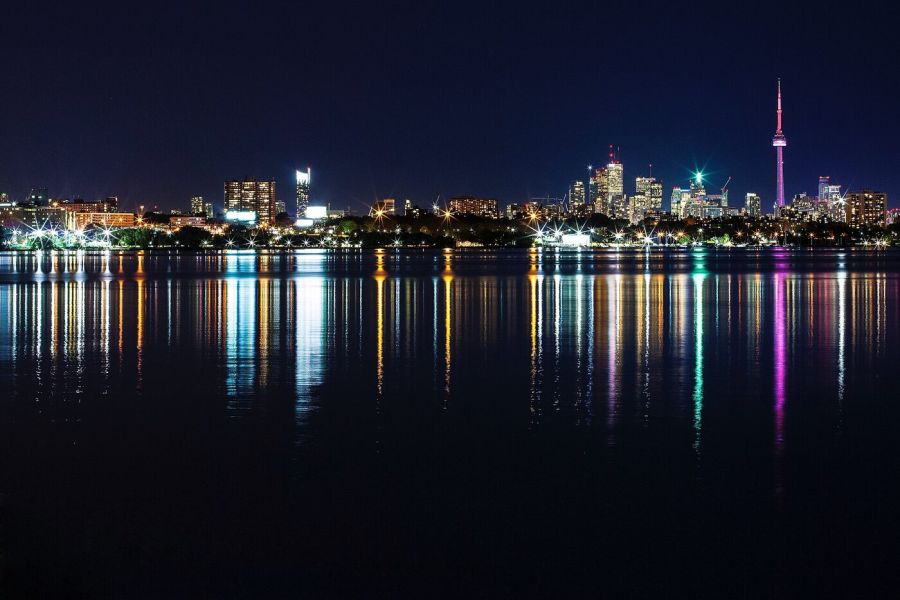 The lights of the Toronto skyline and the slender CN Tower reflected in the dark water of Lake Ontario at night