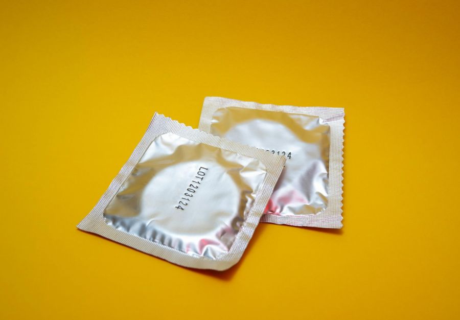 Two condoms in silver foil wrappers on a bright yellow background