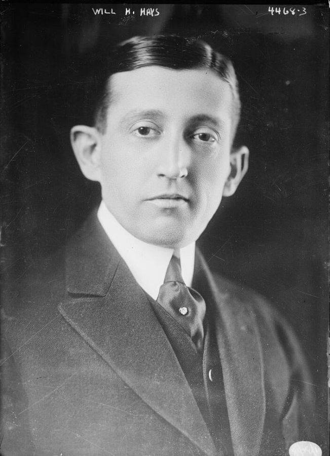 Head and shoulders portrait of a young man with slicked-back dark hair, wearing a dark suit, a high white collar and a patterned tie